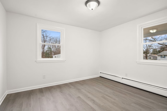 unfurnished room featuring plenty of natural light, light wood-type flooring, and a baseboard heating unit