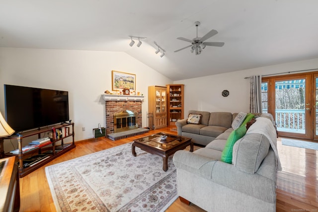 living room with lofted ceiling, a fireplace, light hardwood / wood-style floors, rail lighting, and ceiling fan