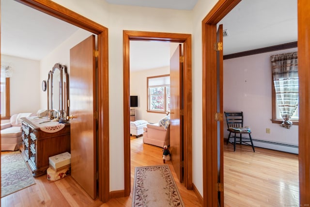 corridor with a baseboard heating unit and light hardwood / wood-style flooring