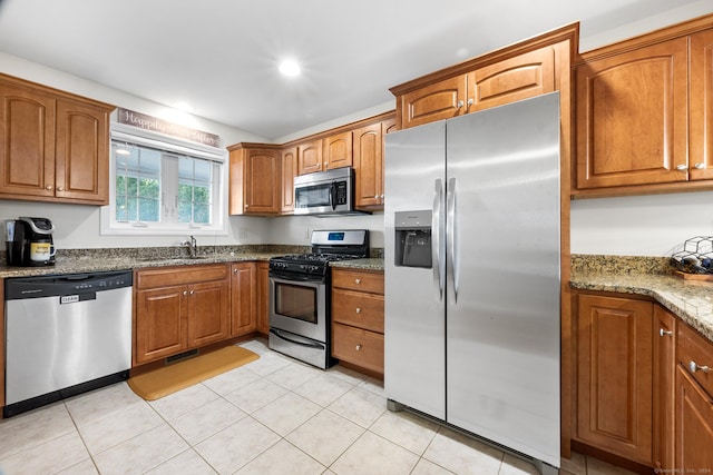 kitchen with light stone countertops, appliances with stainless steel finishes, light tile patterned flooring, and sink