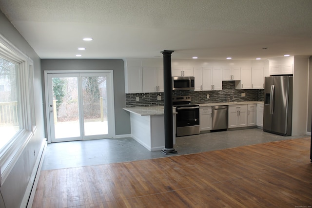 kitchen with stainless steel appliances, a baseboard radiator, backsplash, white cabinets, and hardwood / wood-style flooring