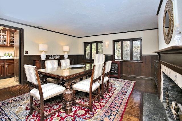 dining space with dark hardwood / wood-style flooring, ornamental molding, a fireplace, and wooden walls