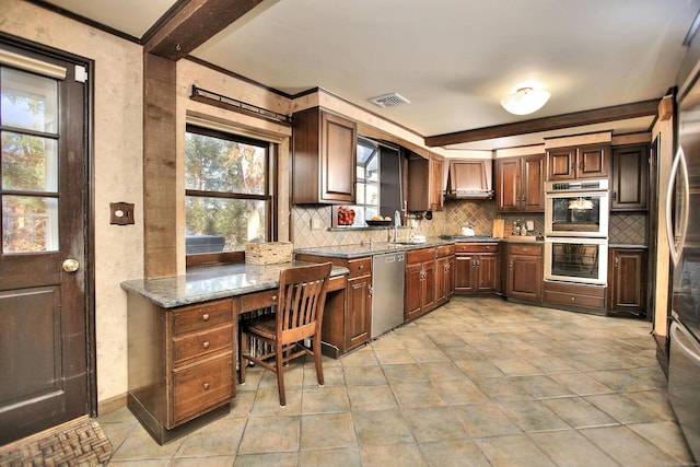 kitchen featuring light stone countertops, wall chimney range hood, decorative backsplash, appliances with stainless steel finishes, and ornamental molding