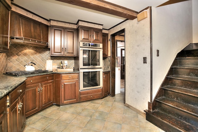 kitchen with tasteful backsplash, beamed ceiling, dark stone counters, light tile patterned floors, and appliances with stainless steel finishes