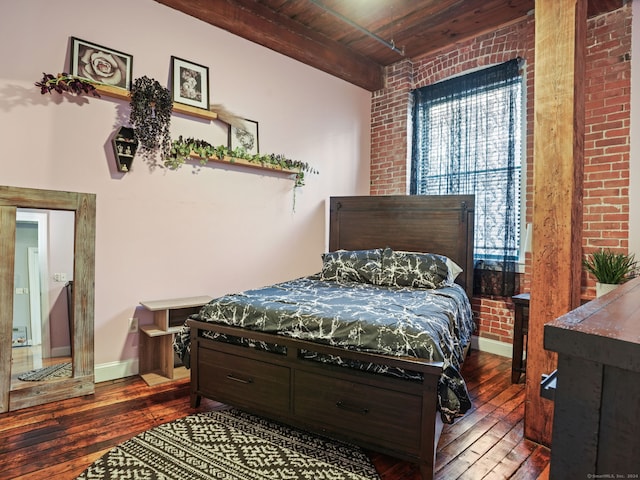 bedroom with brick wall, beamed ceiling, wooden ceiling, and dark hardwood / wood-style floors