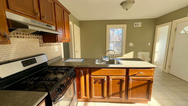 kitchen with backsplash, sink, light tile patterned floors, gas stove, and kitchen peninsula