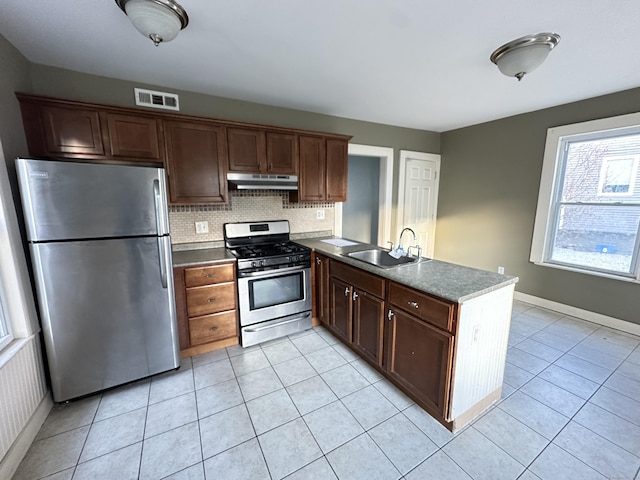 kitchen with kitchen peninsula, appliances with stainless steel finishes, tasteful backsplash, sink, and light tile patterned floors