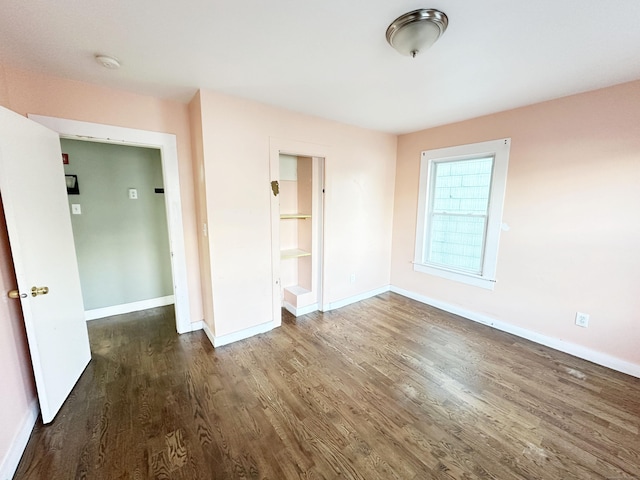 unfurnished bedroom featuring a walk in closet, dark wood-type flooring, and a closet