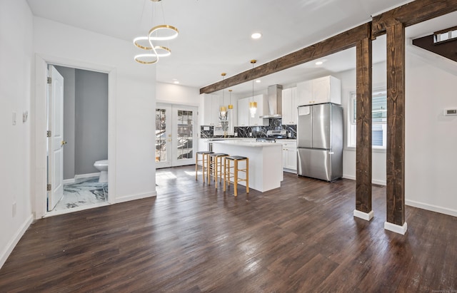 kitchen featuring pendant lighting, a breakfast bar, wall chimney range hood, stainless steel fridge, and white cabinetry