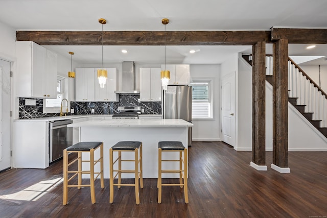 kitchen with wall chimney exhaust hood, stainless steel appliances, decorative light fixtures, white cabinetry, and a kitchen island