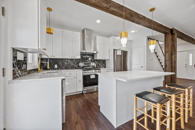 kitchen featuring sink, wall chimney exhaust hood, appliances with stainless steel finishes, beam ceiling, and white cabinetry