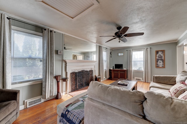 living room with hardwood / wood-style flooring, ceiling fan, ornamental molding, and a textured ceiling