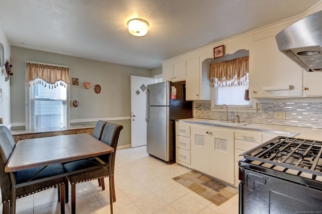 kitchen with stainless steel fridge, white cabinetry, sink, and range hood