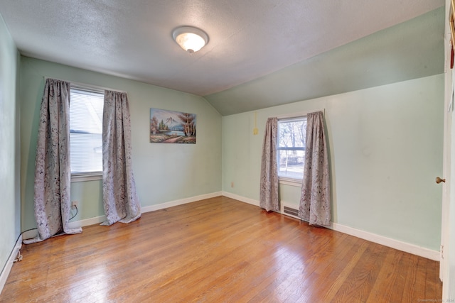 unfurnished room with lofted ceiling, a textured ceiling, a wealth of natural light, and light hardwood / wood-style flooring