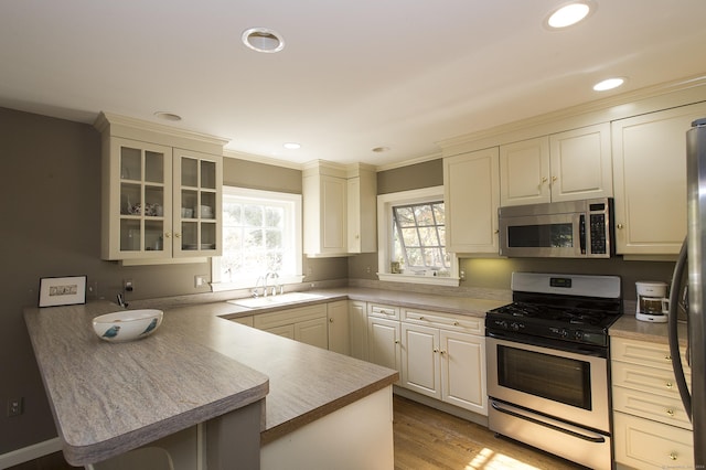 kitchen with sink, kitchen peninsula, stainless steel appliances, and light wood-type flooring