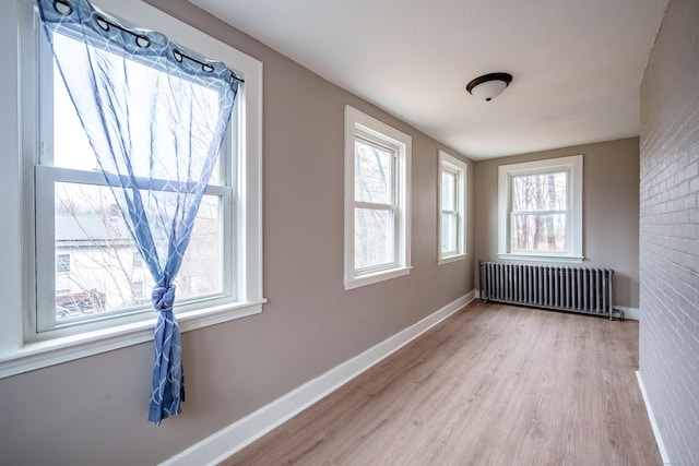 unfurnished room featuring radiator, brick wall, and light wood-type flooring