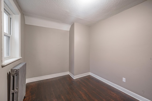 spare room with radiator heating unit, a textured ceiling, plenty of natural light, and dark wood-type flooring