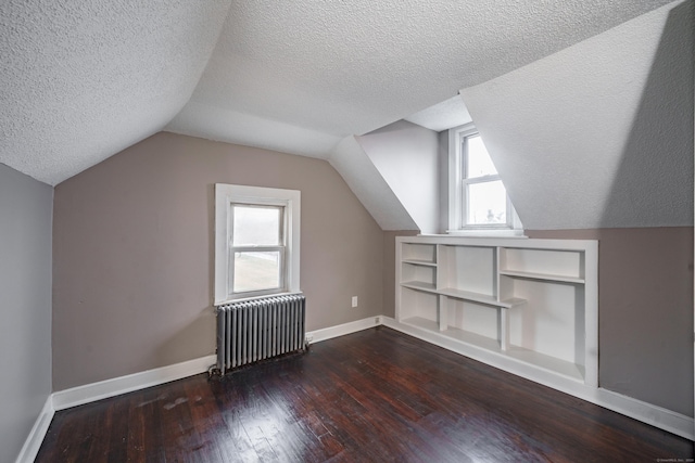 bonus room with dark hardwood / wood-style floors, radiator heating unit, a textured ceiling, and a wealth of natural light