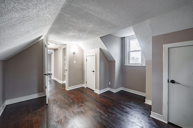 additional living space with a textured ceiling, dark wood-type flooring, and vaulted ceiling