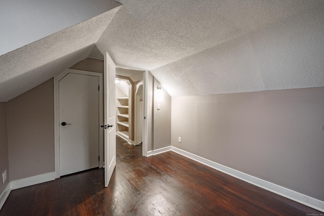 additional living space featuring a textured ceiling, dark hardwood / wood-style flooring, and vaulted ceiling