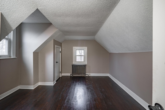 additional living space with vaulted ceiling, radiator, dark hardwood / wood-style flooring, and a textured ceiling