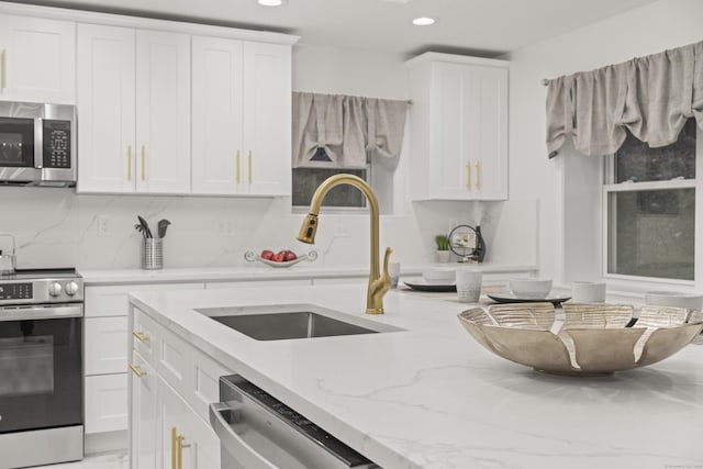 kitchen featuring sink, backsplash, stainless steel appliances, light stone countertops, and white cabinets