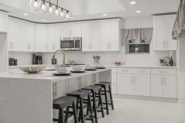 kitchen featuring white cabinetry, hanging light fixtures, a kitchen breakfast bar, light stone countertops, and an island with sink