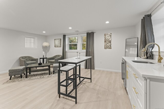 kitchen with white cabinetry, sink, light stone countertops, a healthy amount of sunlight, and light hardwood / wood-style flooring