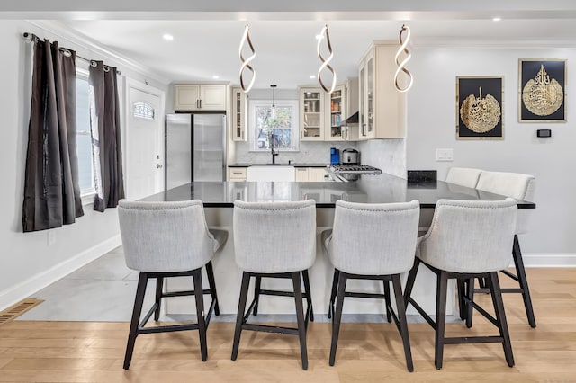 kitchen featuring cream cabinets, a kitchen breakfast bar, stainless steel fridge, decorative light fixtures, and light hardwood / wood-style floors