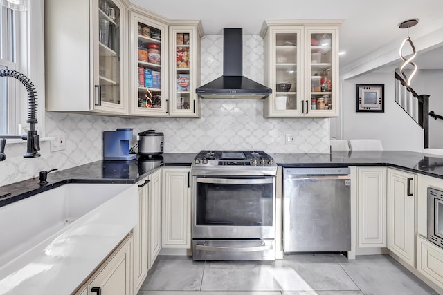 kitchen with cream cabinetry, backsplash, stainless steel appliances, and wall chimney exhaust hood