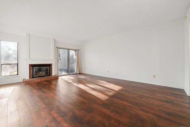 unfurnished living room with dark wood-type flooring, vaulted ceiling, and a brick fireplace