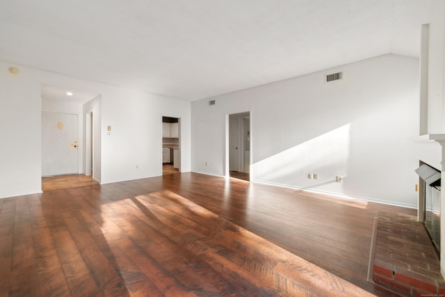 unfurnished living room with dark hardwood / wood-style flooring, a brick fireplace, and lofted ceiling