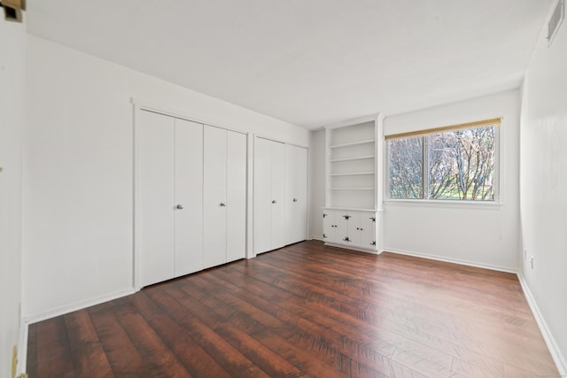 unfurnished bedroom featuring multiple closets and dark wood-type flooring