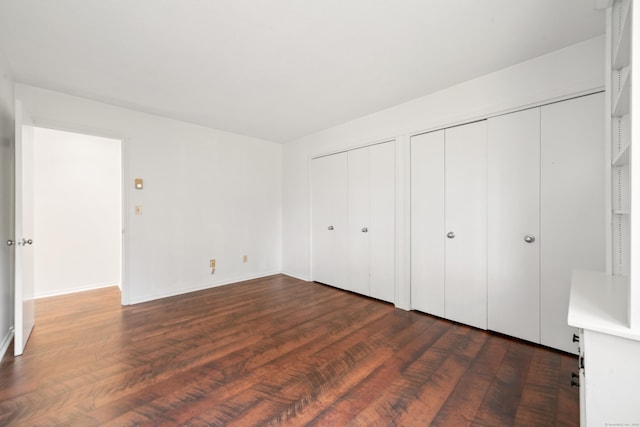 unfurnished bedroom with multiple closets and dark wood-type flooring