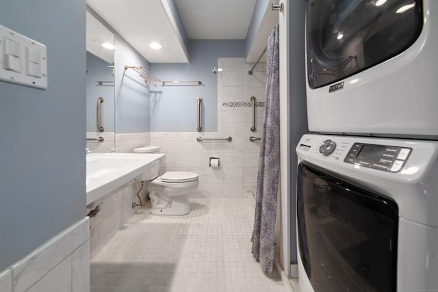 bathroom with curtained shower, stacked washing maching and dryer, tile patterned floors, toilet, and tile walls