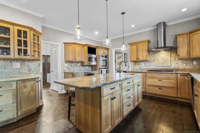 kitchen featuring glass insert cabinets, appliances with stainless steel finishes, wall chimney range hood, a kitchen bar, and a sink