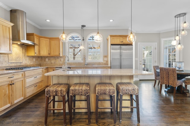 kitchen with light brown cabinets, a kitchen breakfast bar, stainless steel refrigerator, wall chimney exhaust hood, and cooktop