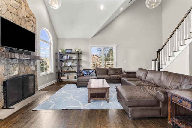 living room with baseboards, wood finished floors, stairs, a fireplace, and high vaulted ceiling