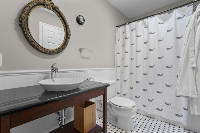 bathroom featuring a shower with shower curtain, wainscoting, vanity, and toilet