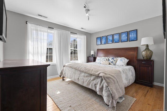 bedroom featuring light wood-style floors, rail lighting, visible vents, and baseboards