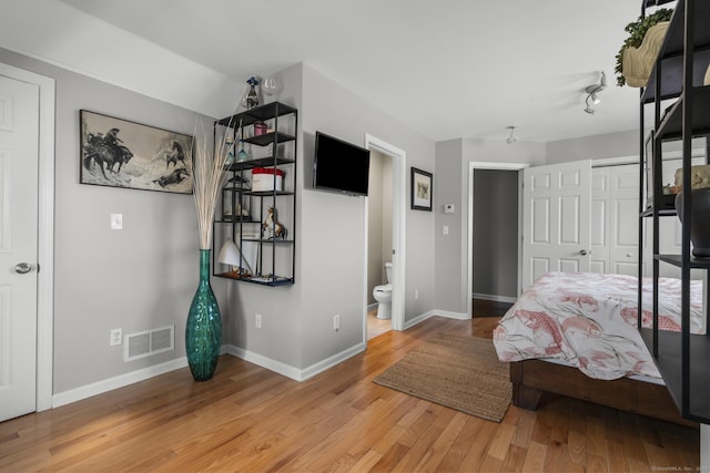 bedroom featuring visible vents, ensuite bathroom, baseboards, and wood finished floors