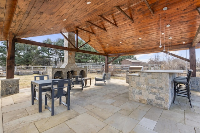 view of patio with outdoor wet bar, an outdoor stone fireplace, area for grilling, fence, and grilling area