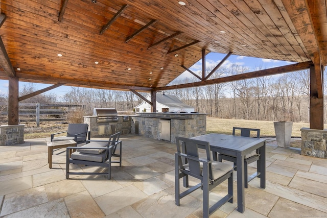 view of patio featuring exterior kitchen, outdoor dining area, a grill, and fence