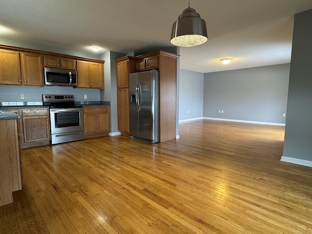 kitchen featuring a textured ceiling, light hardwood / wood-style flooring, decorative light fixtures, and appliances with stainless steel finishes