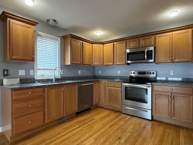 kitchen with a textured ceiling, stainless steel appliances, light hardwood / wood-style floors, and sink