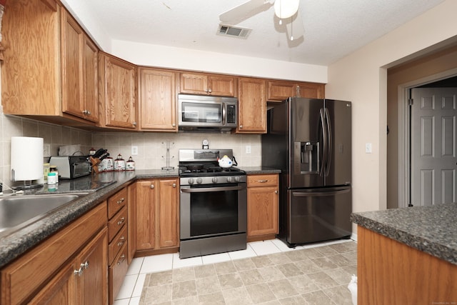 kitchen with ceiling fan, backsplash, a textured ceiling, light tile patterned flooring, and appliances with stainless steel finishes