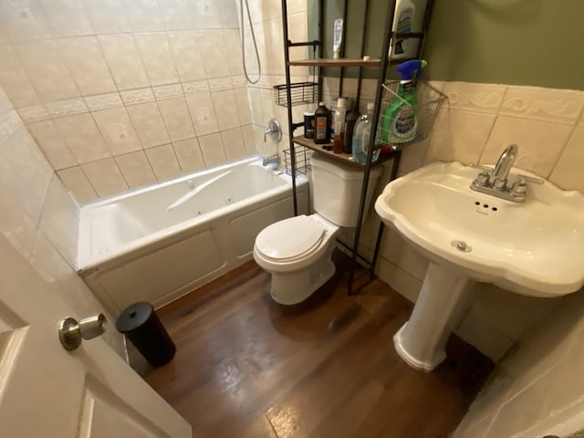 bathroom featuring wood-type flooring, tiled shower / bath combo, toilet, and tile walls