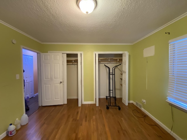 unfurnished bedroom featuring two closets, crown molding, a textured ceiling, and hardwood / wood-style flooring