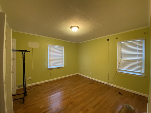 unfurnished room with a textured ceiling, wood-type flooring, and ornamental molding