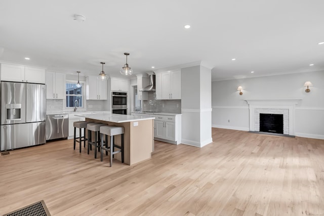 kitchen with hanging light fixtures, stainless steel appliances, a kitchen island, wall chimney range hood, and white cabinets